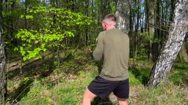 Athletic man trains martial arts outdoors in green forest, performing elbow strikes and boxing moves in slow motion. Strength and discipline in nature.