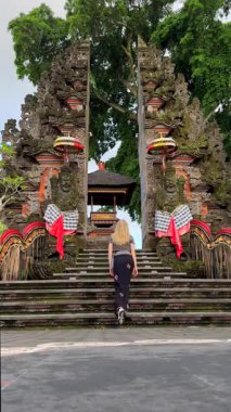 Dişi turist Ubud, Bali 'deki geleneksel Hindu tapınağına merdivenlerden çıkıyor. Süslü taş kapılar, koruyucu heykeller, tören süslemeleri ve kutsal atmosfer..