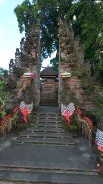 FPV İHA Bali Hindu tapınağına taş heykeller, penjor direkleri ve Endonezya 'daki kutsal kumaşlarla süslü tören kapısından girer. Ruhaniyete ve kültüre sembolik yolculuk.