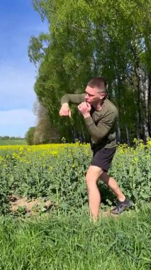 Atletik adam doğada dövüş sanatları yumrukları uyguluyor, yavaş çekimde dinamik boks hareketleri yapıyor, vahşi doğada güç, odaklanma ve disiplin gösteriyor..