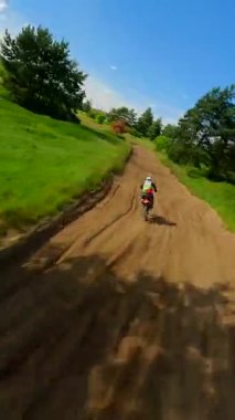 FPV insansız hava aracı yeşil kırsal ve orman boyunca motosiklet sürücüsünü takip ederek yaz güneşinde hızlı dönüşler, hız ve açık hava maceralarını yakalıyor..