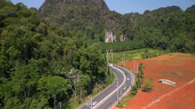Tayland, Krabi 'de manzaralı virajlı yolda giden arabaların hava manzarası, yemyeşil tropikal ormanlar, palmiye tarlaları, kireçtaşı kayalıkları ve renkli araziler arasında kıvrılıyor..