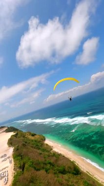 Bali 'deki Pandawa Sahili' nde yamaç paraşütçülerinin kayalıklardan ve turkuaz okyanustan süzülürken çekilmiş sinematik FPV görüntüleri. Manzaralı kıyı şeridi, tropikal dalgalar ve yaz gökyüzü manzarası..