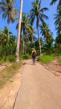 Tropik palmiye ormanlarında koşan sağlıklı bir kadının, güneşli bir günde ağır çekimde çekilmiş sinematik FPV görüntüsü. Fitness, seyahat, refah ve aktif yaşam tarzı temaları için ideal.