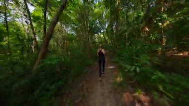 Dinamik FPV kadın drone çekimi verimli tropikal orman yolunda koşuyor, zindelik, özgürlük ve doğa hareketlerini yakalıyor. Refah, seyahat ve macera temaları için ideal.