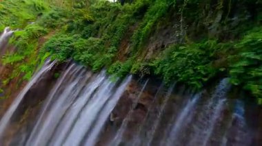 Sinematik FPV insansız hava aracı Doğu Java, Endonezya 'daki yemyeşil yağmur ormanları uçurumlarıyla çevrili çok akımlı Tumpak Sewu şelalesine dalarken çekildi..