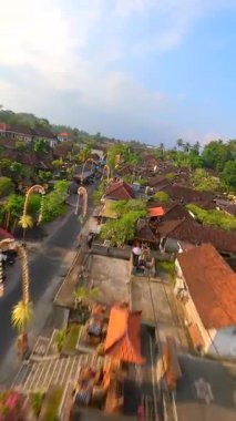 Endonezya 'nın Bali kentindeki bereketli tropikal yeşilliklerle çevrili geleneksel Bali köyündeki dekore edilmiş cadde üzerinde FPV insansız hava aracı uçuşu