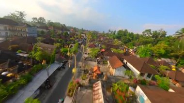Endonezya 'nın Bali kentindeki bereketli tropikal yeşilliklerle çevrili geleneksel Bali köyündeki dekore edilmiş cadde üzerinde FPV insansız hava aracı uçuşu