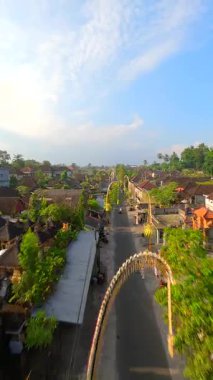 Endonezya 'nın Bali kentindeki bereketli tropikal yeşilliklerle çevrili geleneksel Bali köyündeki dekore edilmiş cadde üzerinde FPV insansız hava aracı uçuşu