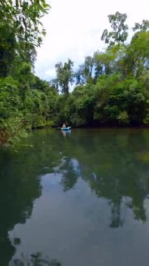Tayland 'da yemyeşil bir ormanda tropikal nehirde kayak yapan bir kadının FPV görüntüsü. Huzurlu, sinematik doğa manzarası seyahat, eko-turizm ve açık hava yaşam tarzı projeleri için ideal.