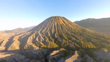 Bromo Dağı yakınlarındaki Batok Dağı 'nın sinematik hava manzarası. Endonezya, Doğu Java 'da engebeli volkanik dokular ve ılık sabah ışığı.