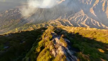 Gündoğumunda Bromo Dağı 'nın volkanik yamaçları ve krateri üzerinde uçan FPV insansız hava aracı Doğu Java, Endonezya' daki kalderadan yükselen buharla birlikte.