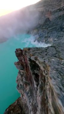 Sinematik FPV insansız hava aracı İjen volkanı krater gölü, Doğu Java 'ya çarpıcı sülfür buharı ve canlı turkuaz suyla uçuyor. Çiğ jeoloji, gerçeküstü manzara ve volkanik güzellik..