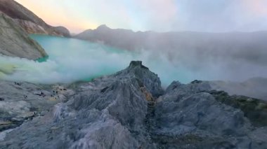 Sinematik FPV insansız hava aracı İjen volkanı krater gölü, Doğu Java 'ya çarpıcı sülfür buharı ve canlı turkuaz suyla uçuyor. Çiğ jeoloji, gerçeküstü manzara ve volkanik güzellik..