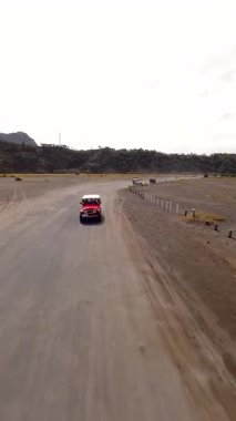 Doğu Java, Endonezya 'daki Bromo Dağı yakınlarındaki volkanik siyah kum ovalarından geçen off-road araçlarının sinematik FPV görüntüleri. Seyahat, tur ve macera kavramı.