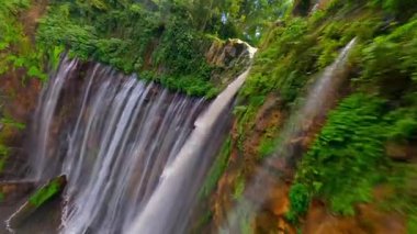 Sinematik FPV insansız hava aracı Doğu Java, Endonezya 'daki yemyeşil yağmur ormanları uçurumlarıyla çevrili çok akımlı Tumpak Sewu şelalesine dalarken çekildi..