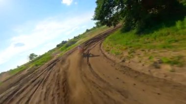 Motokros sürücüsünün toprak yolda döndüğü FPV 'nin sinematik yavaş çekim görüntüleri. Toz uçuşu, dinamik kıvrımlar ve doğal yaz manzarasında güçlü hareketler..