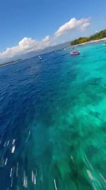 Tropikal Gili Trawangan, Endonezya üzerinde dinamik FPV insansız hava aracı uçuşu, turkuvaz denizi, botlar, beyaz kum plajı ve mercan resifleri. Ada cennetinin göz kamaştırıcı manzarası.