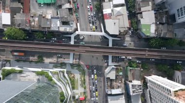 Bangkok, Tayland 'da işlek caddenin üzerinde BTS Skytrain raylarının yukarıdan aşağı havadan görüntüsü. Arabalar, binalar ve yükseltilmiş demiryolu altyapısı ile şehir ulaşımı sahnesi.