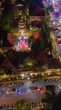 Orta Ubud, Bali 'nin hava gece görüşü, kalabalık sokak trafiği ve açık hava sahnesindeki geleneksel kültürel performans, canlı ışıklar ve tropikal bahçelerle çevrili..