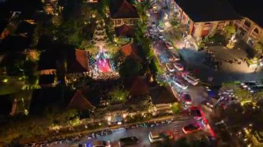 Orta Ubud, Bali 'nin hava gece görüşü, kalabalık sokak trafiği ve açık hava sahnesindeki geleneksel kültürel performans, canlı ışıklar ve tropikal bahçelerle çevrili..
