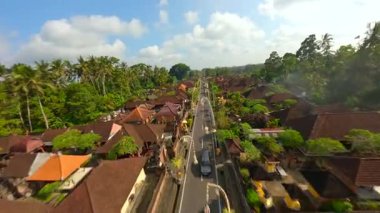 Endonezya 'nın Bali kentindeki bereketli tropikal yeşilliklerle çevrili geleneksel Bali köyündeki dekore edilmiş cadde üzerinde FPV insansız hava aracı uçuşu