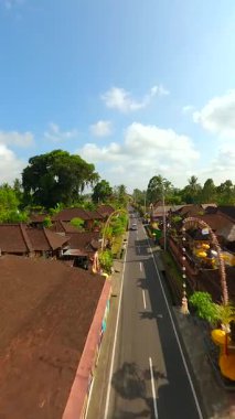 Endonezya 'nın Bali kentindeki bereketli tropikal yeşilliklerle çevrili geleneksel Bali köyündeki dekore edilmiş cadde üzerinde FPV insansız hava aracı uçuşu