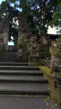 Bali 'nin Ubud kentindeki süslü Bali tapınağının sinematik FPV manzarası, yosun kaplı taş oymalar, heykeller ve geleneksel mimari.