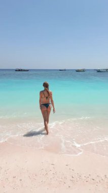 Bikinili bir kadının kumlu tropikal plajda turkuaz denize doğru yürüdüğünü hayal edin. Yaz havası, berrak su ve Asya 'daki egzotik kıyı gezisi sahnesi..