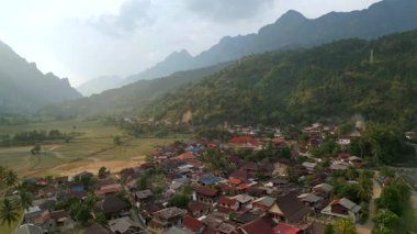 Yeşil pirinç tarlaları, tropikal bitki örtüsü ve arka planda dramatik kireçtaşı dağlarıyla çevrili Vang Vieng, Laos yakınlarındaki geleneksel köyün hava manzarası. Gün batımında Asya manzarası.