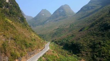 Kuzey Vietnam 'daki Ha Giang dağları boyunca sarmal yol manzarası sarp yeşil tepeler ve keskin kireçtaşı zirveleriyle çevrili..