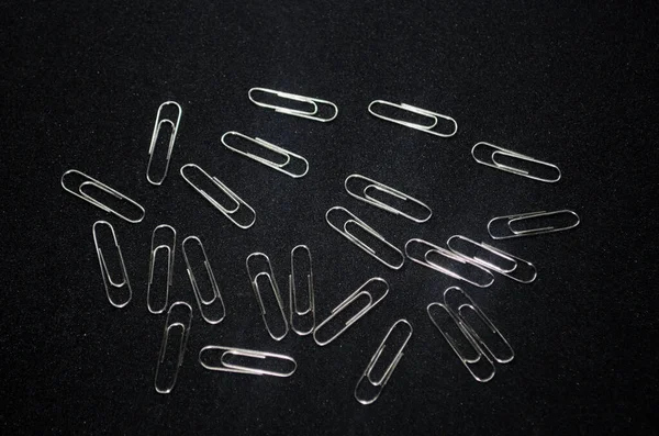 many metal clips in the shape of a paper on a black background. office equipment, stationery and tools for work. office supplies