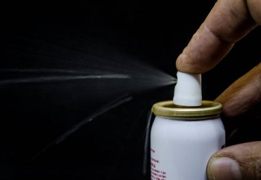 Püskürten bir adamın yakın görüntüsü, siyah bir arka planda elinde bir sprey kutusu.