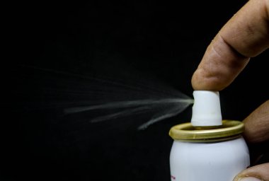 Püskürten bir adamın yakın görüntüsü, siyah bir arka planda elinde bir sprey kutusu.