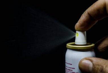 Püskürten bir adamın yakın görüntüsü, siyah bir arka planda elinde bir sprey kutusu.