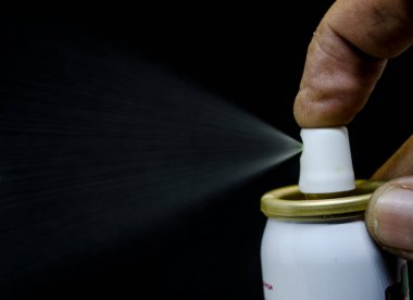 Püskürten bir adamın yakın görüntüsü, siyah bir arka planda elinde bir sprey kutusu.