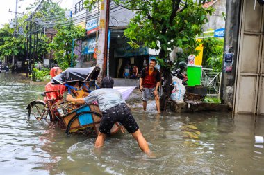 Semarang, Aralık 2022. Bazı insanlar, Poncol tren istasyonundaki selde mahsur kalan insanları taşıyan pedikürleri itiyor..