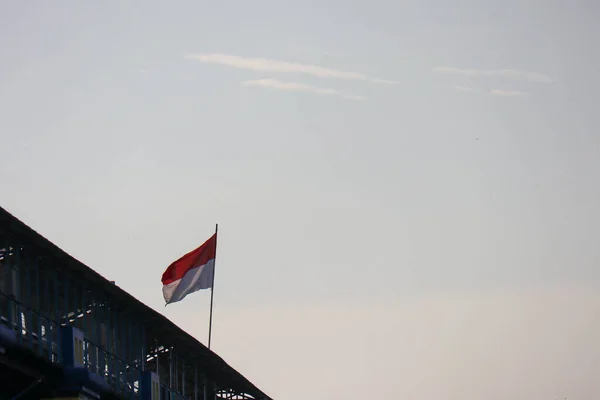 The Indonesian red and white flagpole flutters against a cloudy sky background