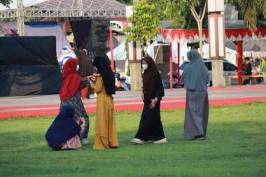 Kudus, December 2022. Photograph of visitors sitting relaxed enjoying the afternoon on the grass of the Kudus city square.
