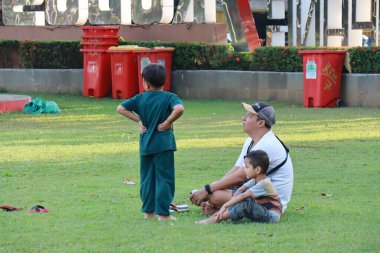 Kudus, December 2022. Photograph of visitors sitting relaxed enjoying the afternoon on the grass of the Kudus city square.