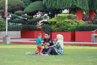Kudus, December 2022. Photograph of visitors sitting relaxed enjoying the afternoon on the grass of the Kudus city square.