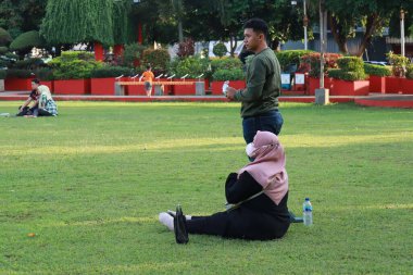 Kudus, December 2022. Photograph of visitors sitting relaxed enjoying the afternoon on the grass of the Kudus city square.