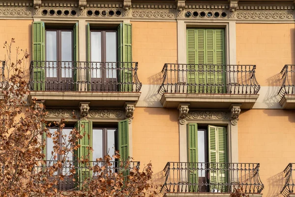 Traditional Barcelona style balconies and green wooden shuttered windows on facade of the renovated house on a sunny day, in the old city of the center.