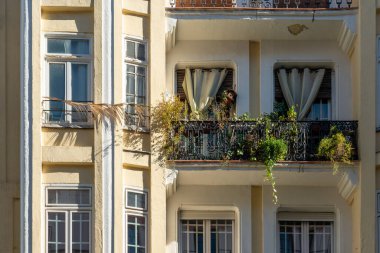 The facade of typical Spanish old house with beautiful balcony with various green plants in sunny winter day. Balcony with curtains and metal railings.