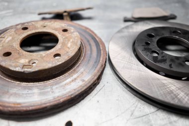 Old rusty brake disc and new disc. Change the old to new brake disc on car in a garage. Auto repair concept