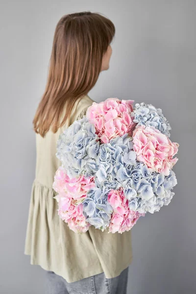 Florist woman creates beautiful bouquet with blue and pink hydrangea. European floral shop concept. Handsome fresh bunch. Education, master class and floristry courses. Flowers delivery.. High