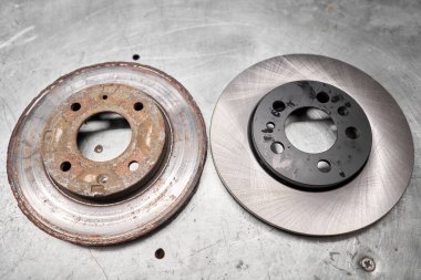 Old rusty brake disc and new disc. Change the old to new brake disc on car in a garage. Auto repair concept