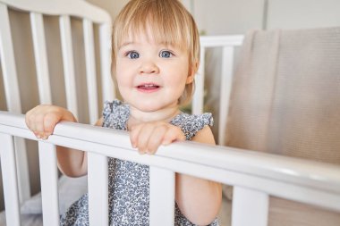  Beşikte duran mutlu bir buçuk bebek. Güneşli yatak odasında oyuncak maymunla oynayan 18 aylık bir çocuk. Ebeveyn yatak odasında bebek karyolası. Yüksek kalite fotoğraf