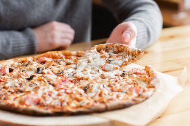 Closeup hand of chef baker in uniform blue apron cutting pizza at kitchen. High quality photo