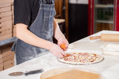 Closeup hand of chef baker in uniform blue apron cutting pizza at kitchen. High quality photo